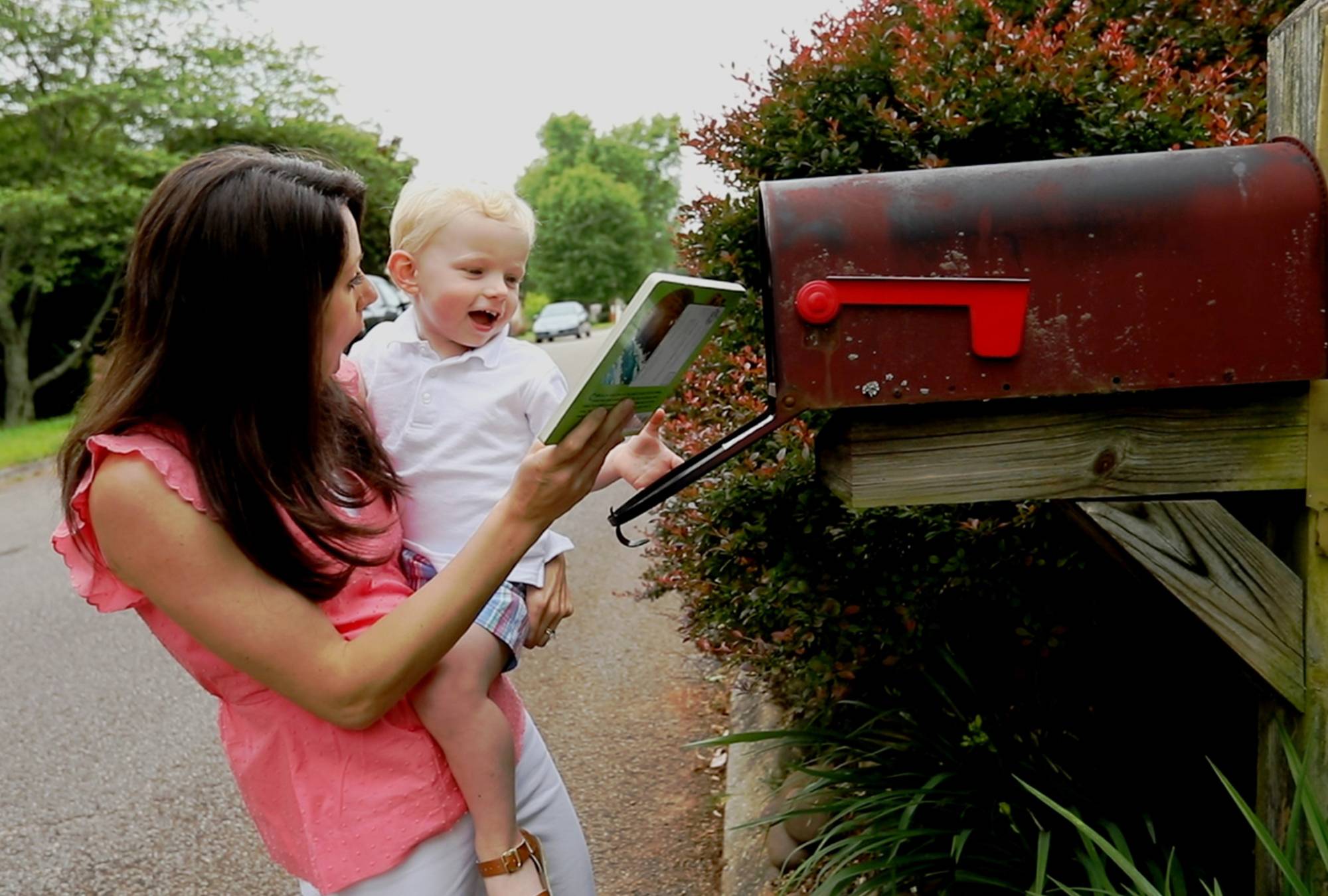 Mom holding young son and opening mailbox to receive Imagination Library book 