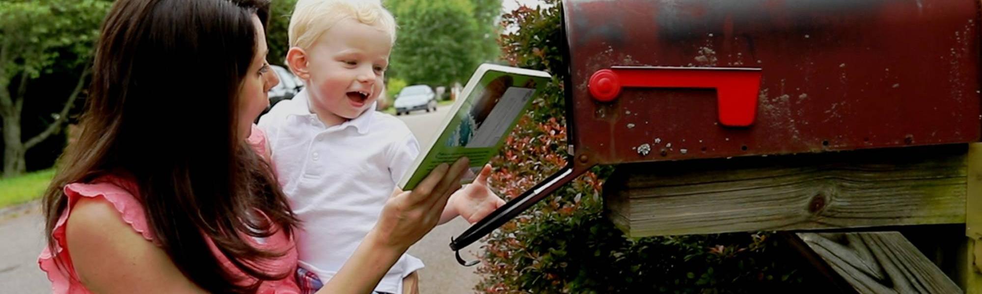 Mom holding young son and opening mailbox to receive Imagination Library book 