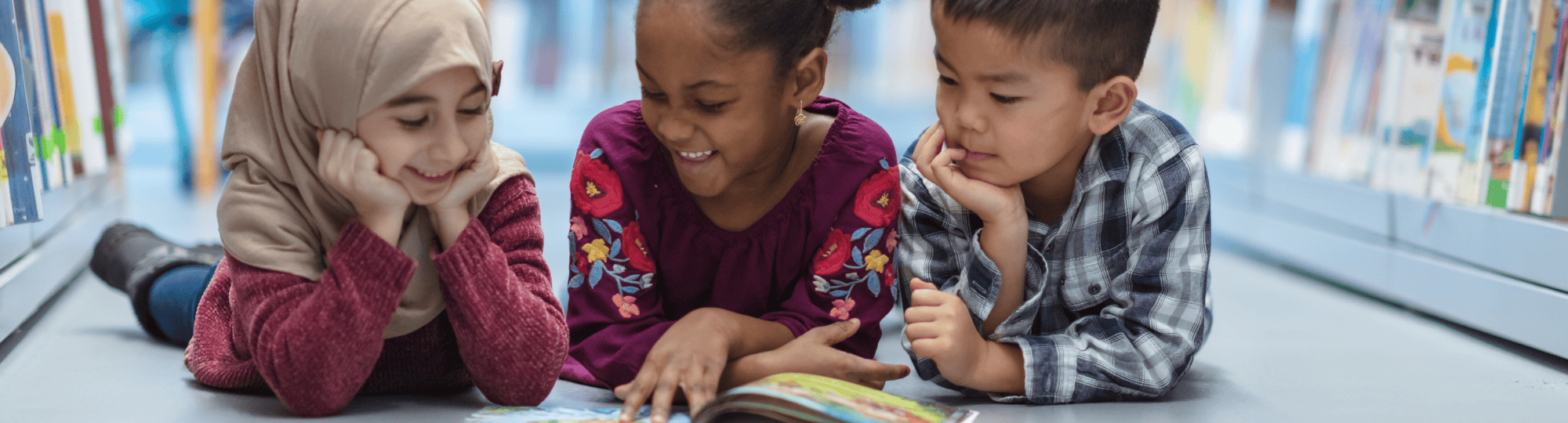 3 kids of mixed races smiling and looking at a book
