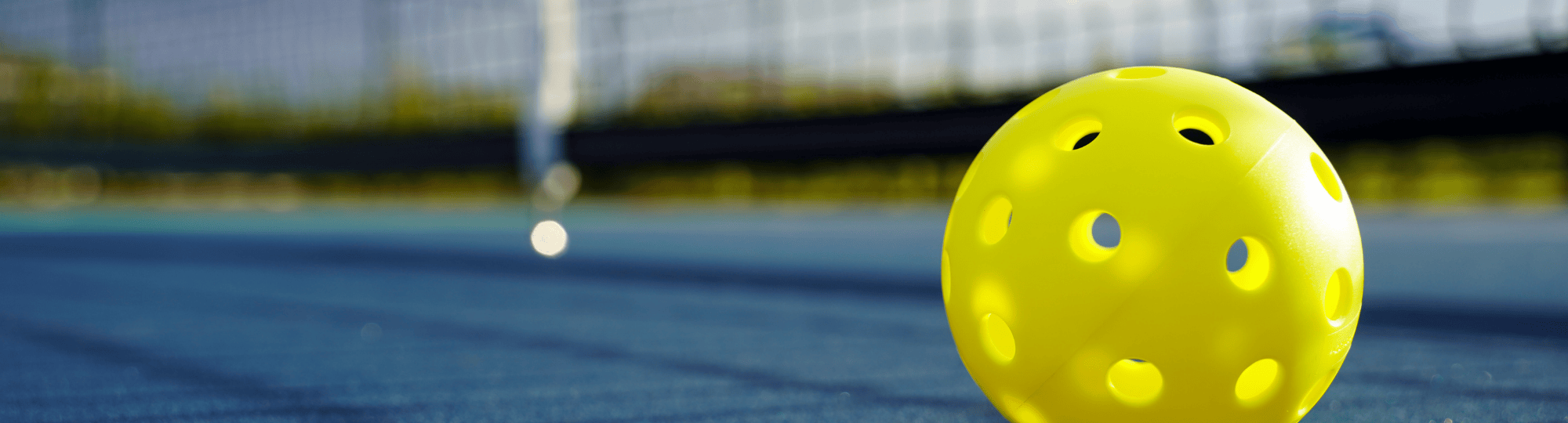 large yellow pickleball in foreground with pickleball court in background