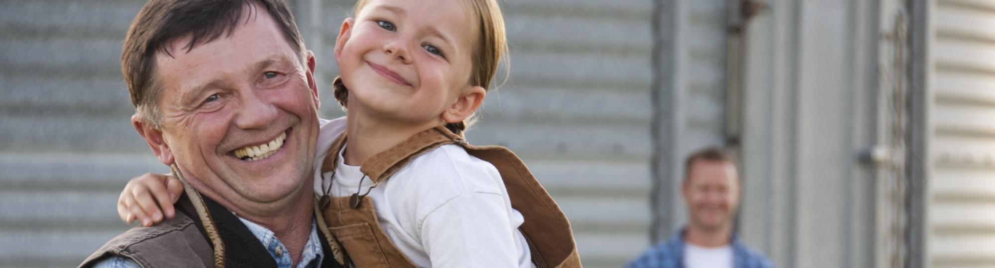 Middle-aged man carrying girl in overalls on farm