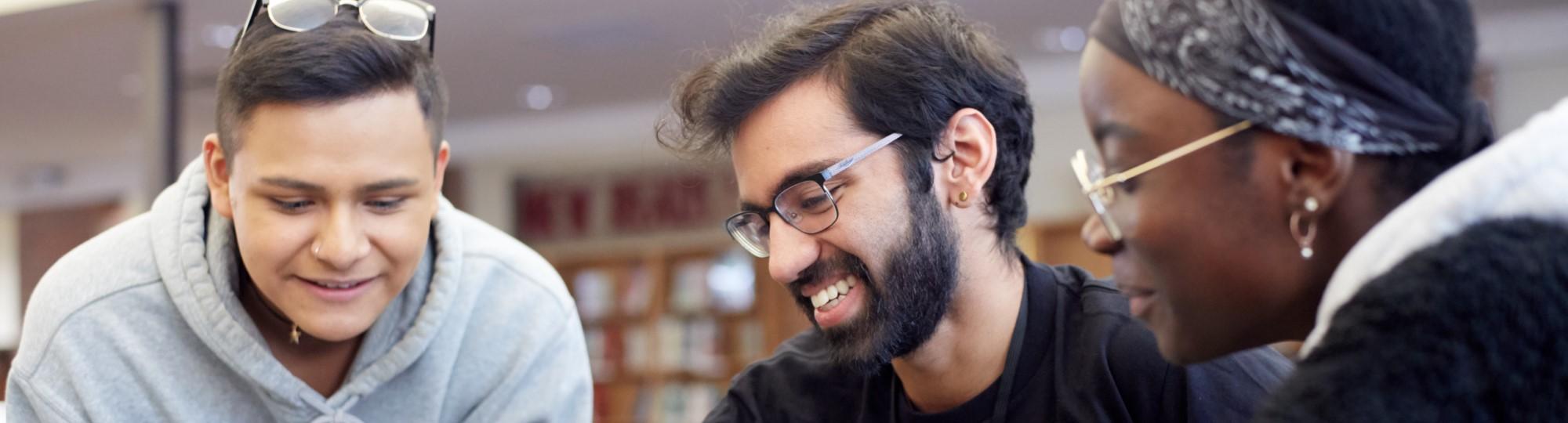 Three young adults are looking at something in a library.