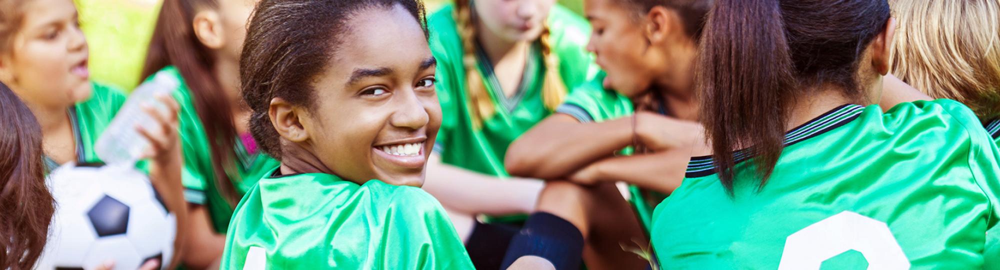 Girls in bright green soccer jerseys, one turning to the camera and smiling