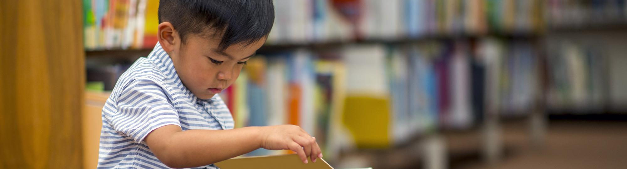 A boy sitting on a stack of books reading