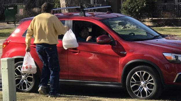 Community Cafe volunteer delivers to-go meals to the open window of a red car