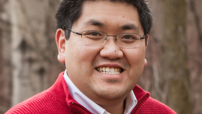 Gordon wears a red shirt and smiles at the camera