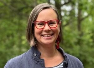Rachel wears red glasses and smiles at the camera