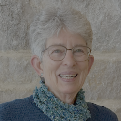 Anne wears glasses and smiles at the camera