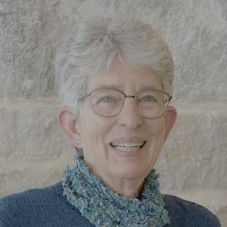 Anne wears glasses and smiles at the camera