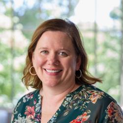 Katie wears a floral blouse and smiles at the camera